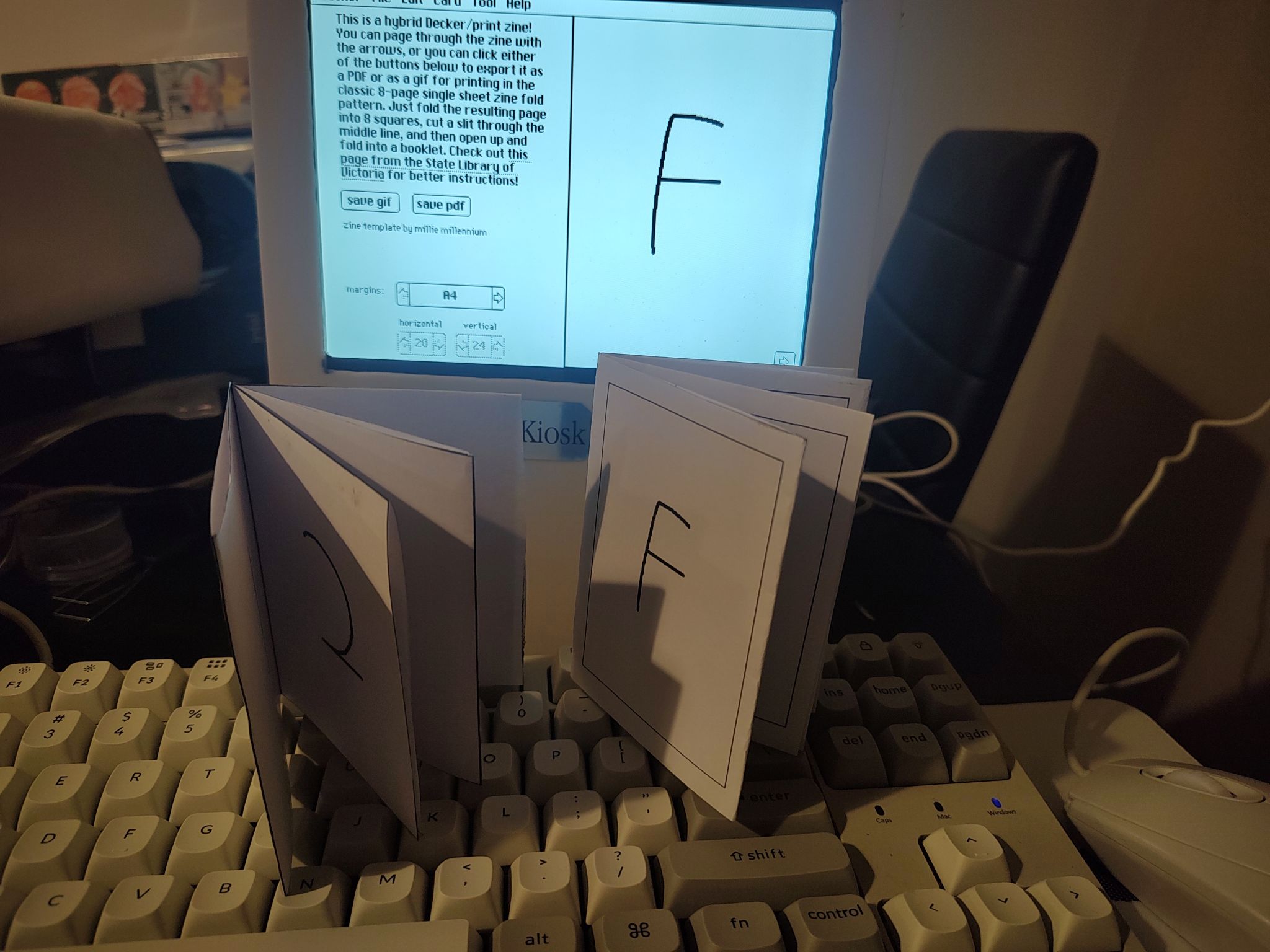 Two print zines sitting in front of the Deck Kiosk displaying the same zine on its screen