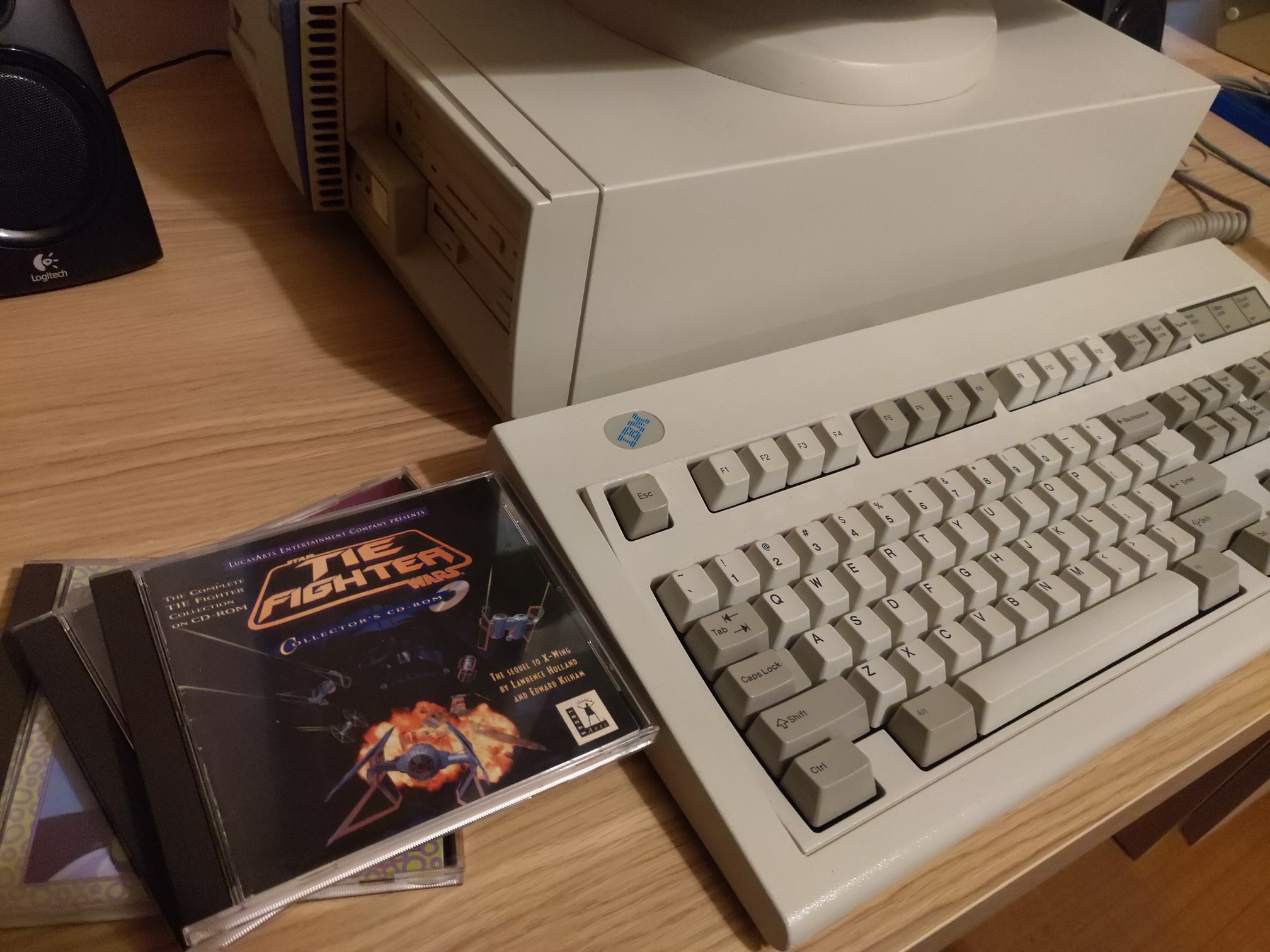An IBM computer, an IBM Model M keyboard, and a pile of CD-ROMs with TIE Fighter on top